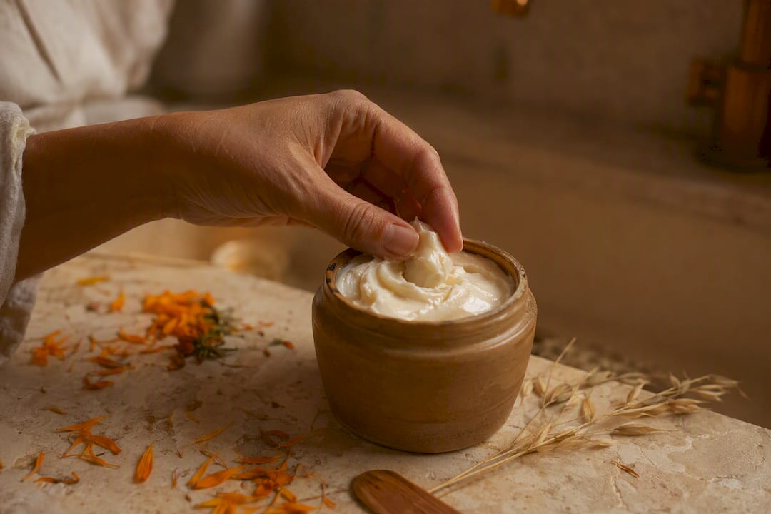 Hand scooping natural cream from jar with botanicals