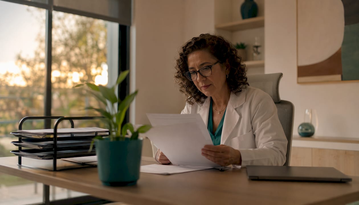 Médica revisando expedientes en su consultorio con el portátil