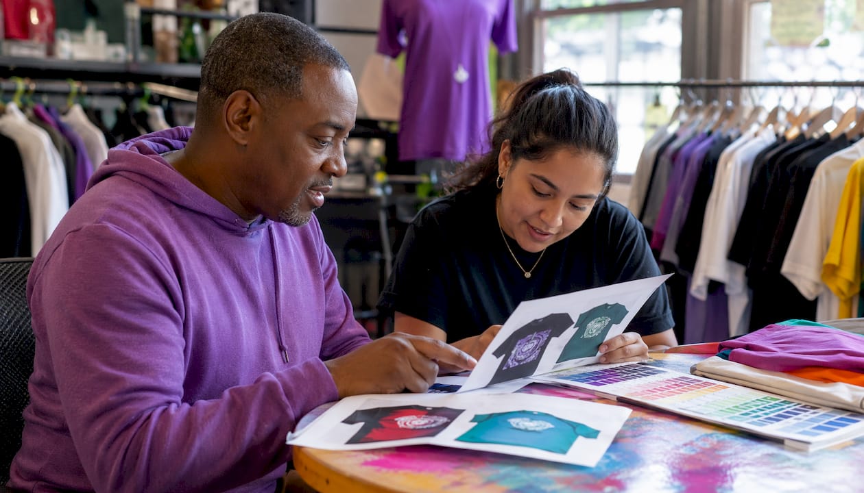 Two print shop workers discussing custom t-shirts