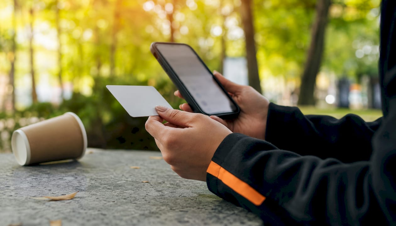 Hands holding insurance card and smartphone at café table