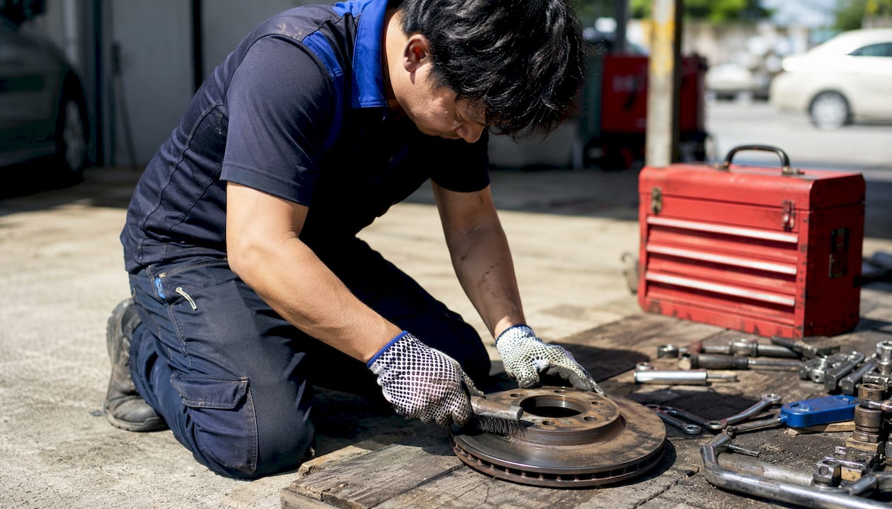 Hands cleaning rusty brake rotor with wire brush