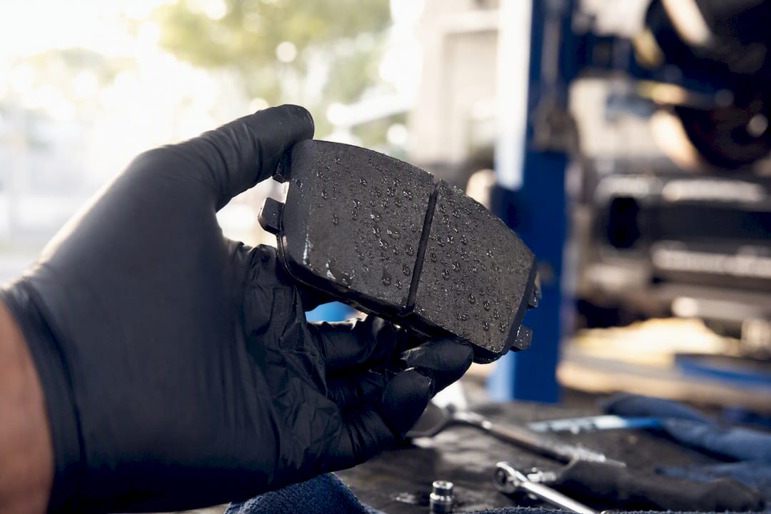 Gloved hand holding moist brake pad showing water droplets