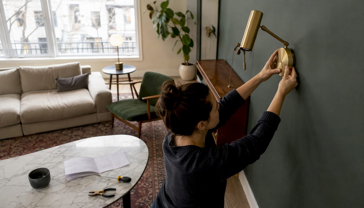 Woman installing brass swing-arm sconce in bedroom