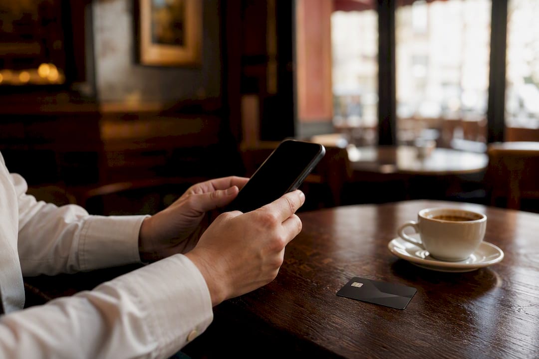 Mains utilisant un smartphone et une carte bancaire près d'un expresso