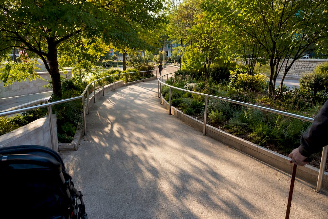 Rampe d'accès pour personnes à mobilité réduite dans un parc parisien avec un déambulateur et une poussette en partie visibles