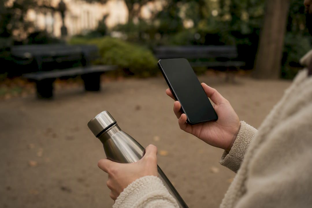 Hands holding smartphone and coffee cup outdoors