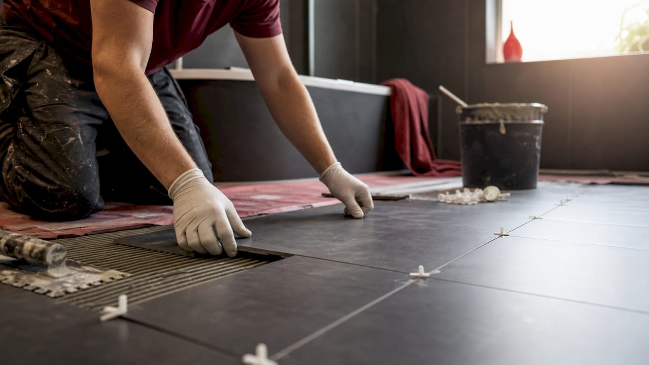 Hands installing matte porcelain tile in bathroom