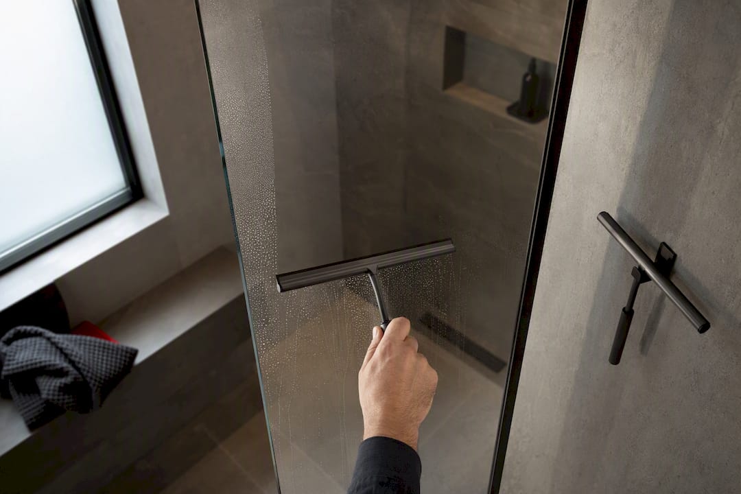Hand squeegeeing water from shower glass
