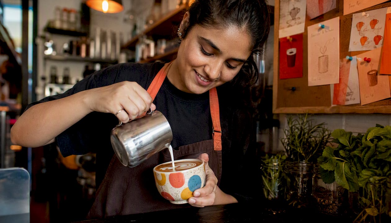 Barista pouring oat milk into chai latte at café
