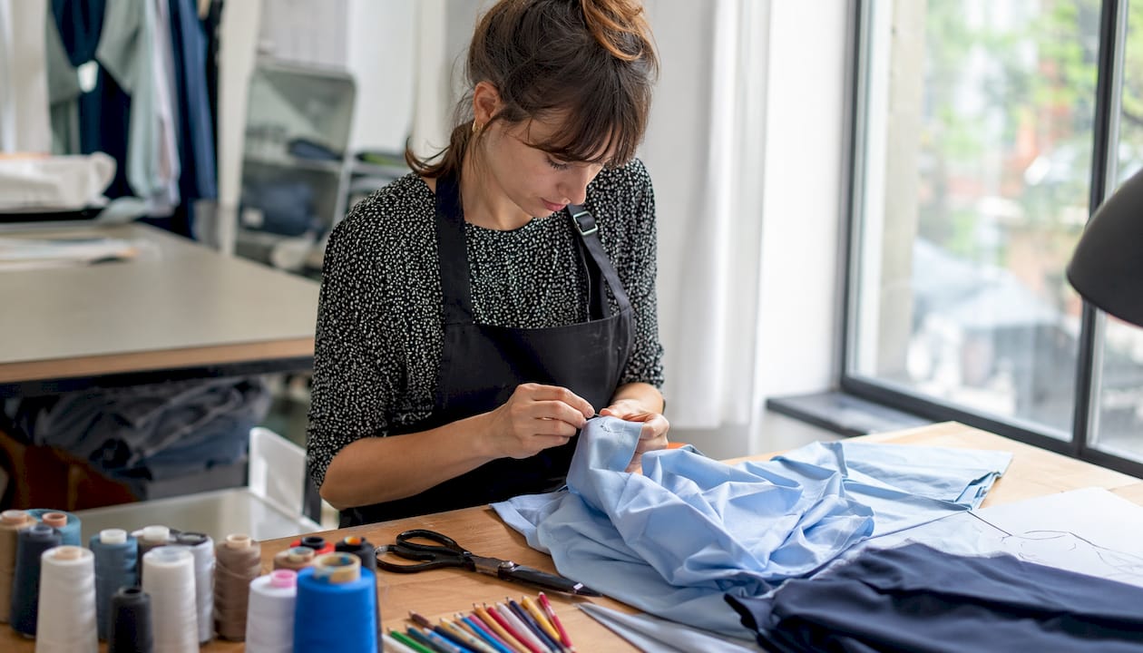 Eine Frau bringt ein kleines Logo per Hand auf den Ärmel eines T-Shirts an.