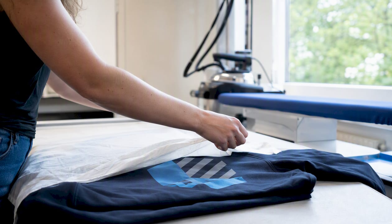 Eine Hand legt ein Tuch auf den Hoodie, um ihn vor dem Bügeln zu schützen.