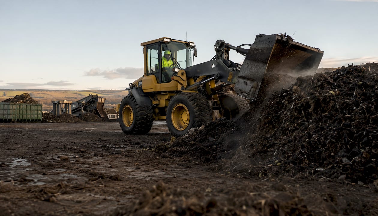 Worker operating machinery at industrial compost facility