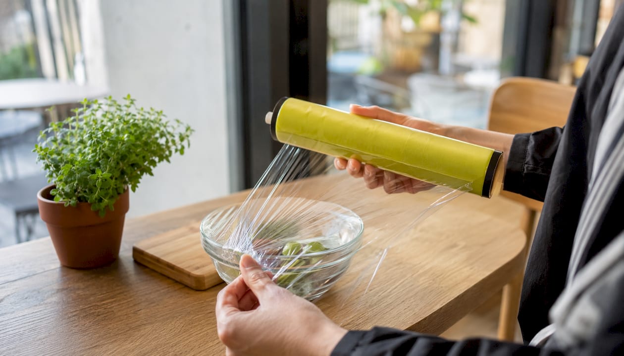 Hands using certified compostable cling wrap roll