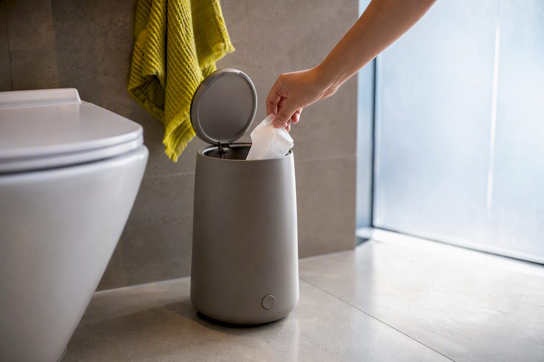 Hand placing wipe into lidded bathroom bin