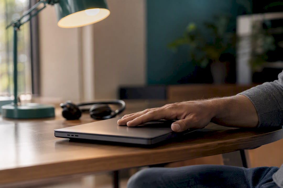 Hand poised over laptop with headset nearby