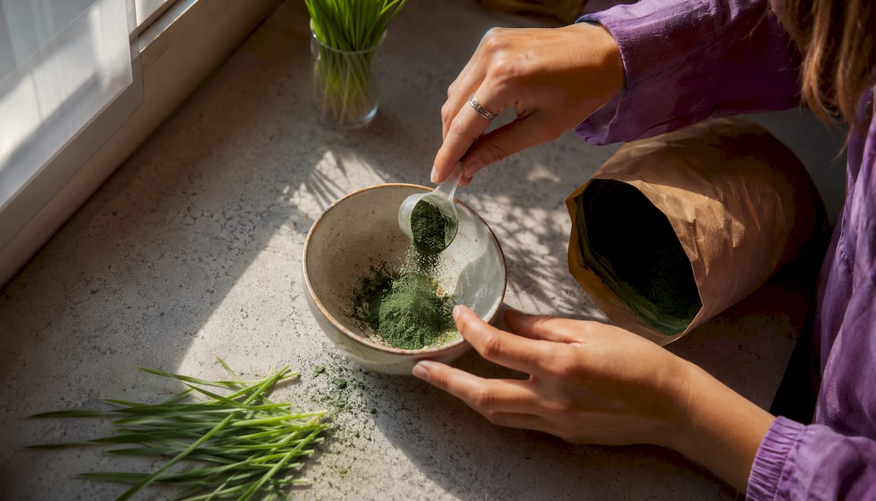 Hands holding greens powder scoop at kitchen table