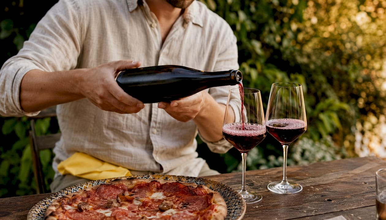 Hands holding Lambrusco near pepperoni pizza