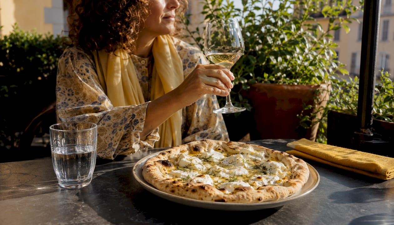 Woman enjoying white pizza with white wine outdoors