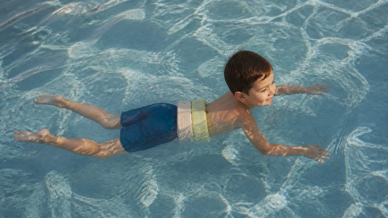 Ein Kind liegt mit einem Schwimmgürtel entspannt waagerecht im Pool und genießt das Wasser.