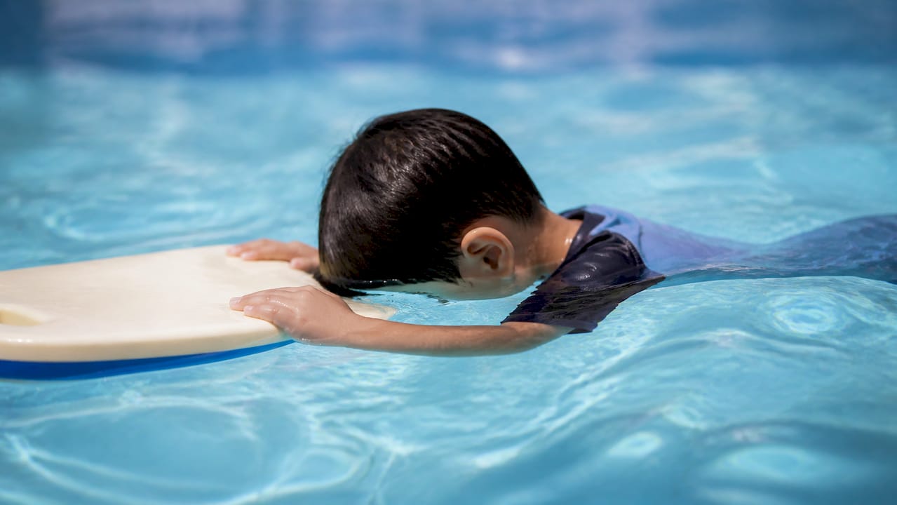 Kind legt die Stirn aufs Wasser mit Schwimmbrett