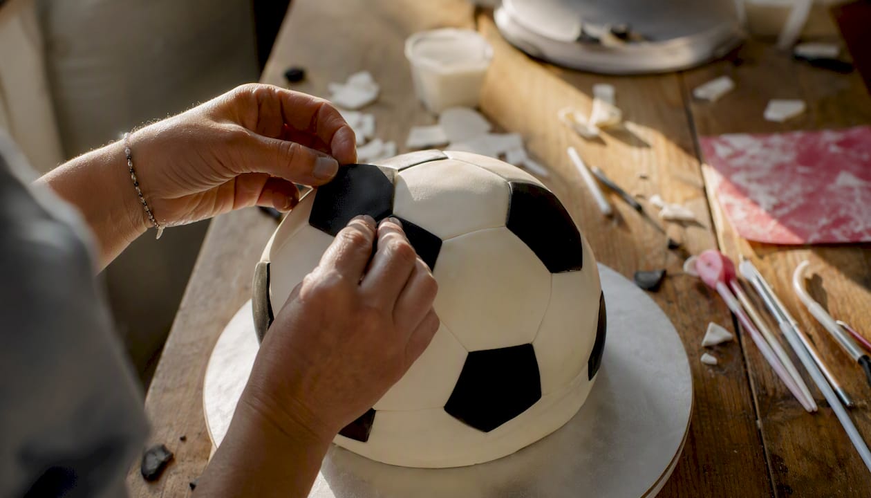 Mit geschickten Händen wird eine Fußballtorte liebevoll mit Fondant verziert.