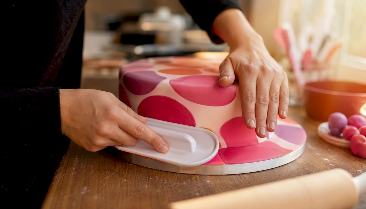 Mit einem Fondantglätter werden die Ränder des Fondants auf der Torte sorgfältig geglättet.