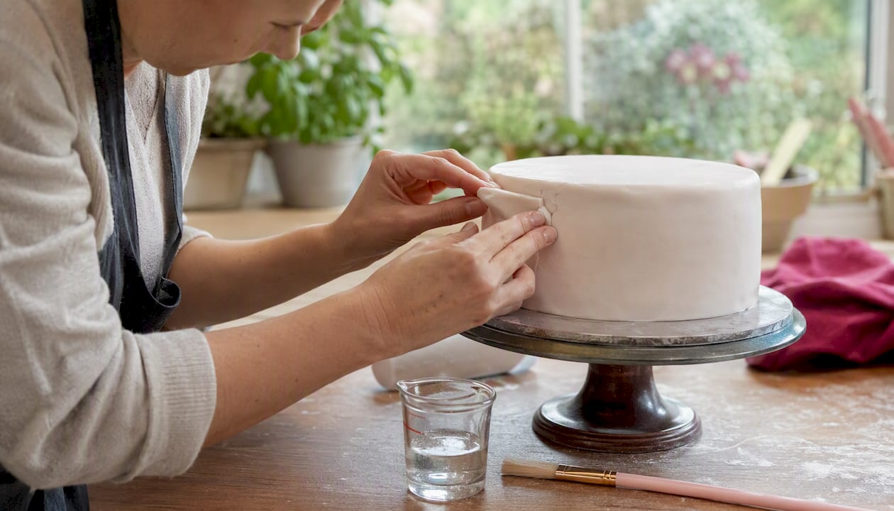 Mit geschickten Händen wird eine eingerissene Fondantschicht auf der Torte sorgfältig ausgebessert.
