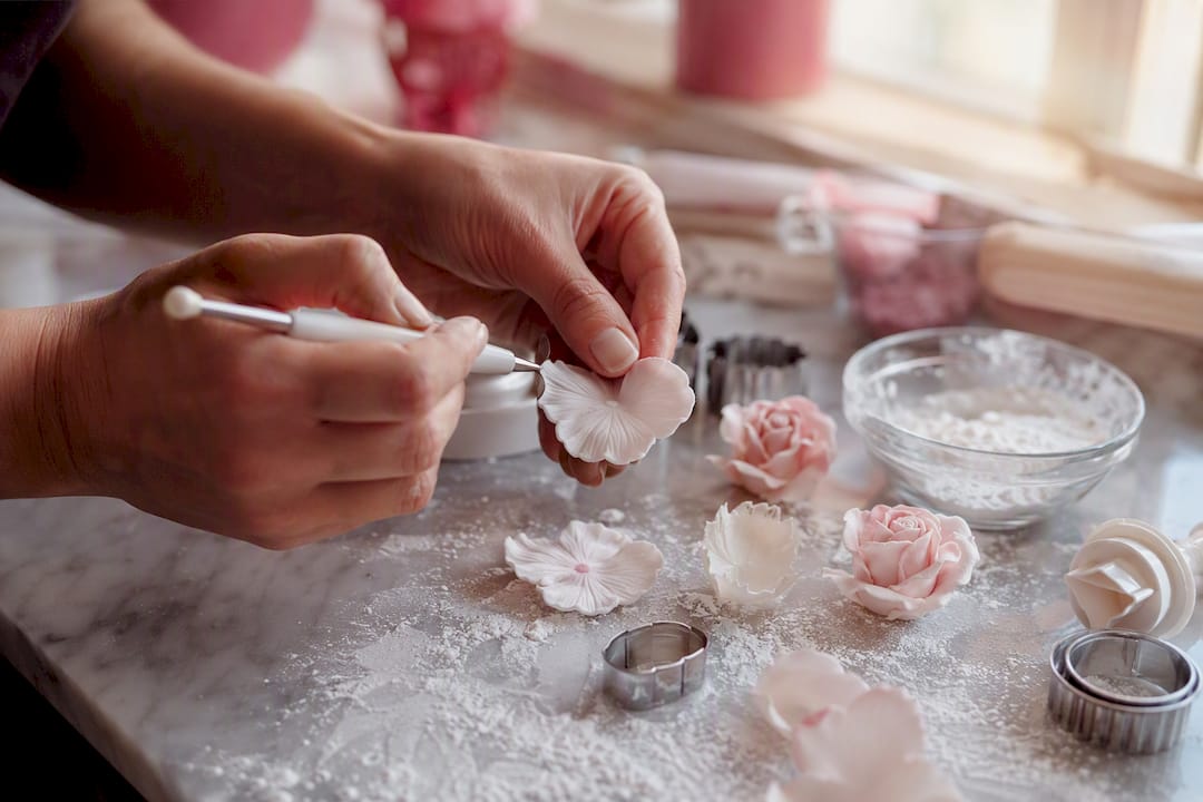 Mit viel Fingerspitzengefühl formen Hände filigrane Blumen aus Zuckermasse.
