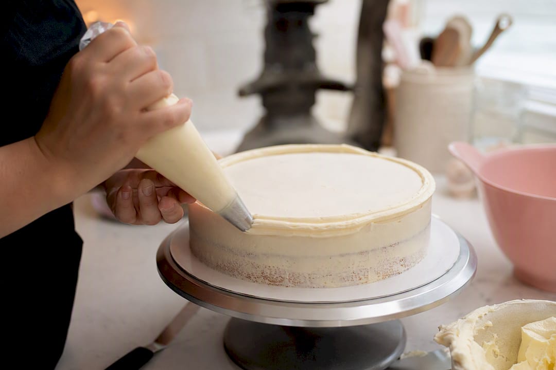Hände spritzen Buttercreme-Rand um den Tortenumfang