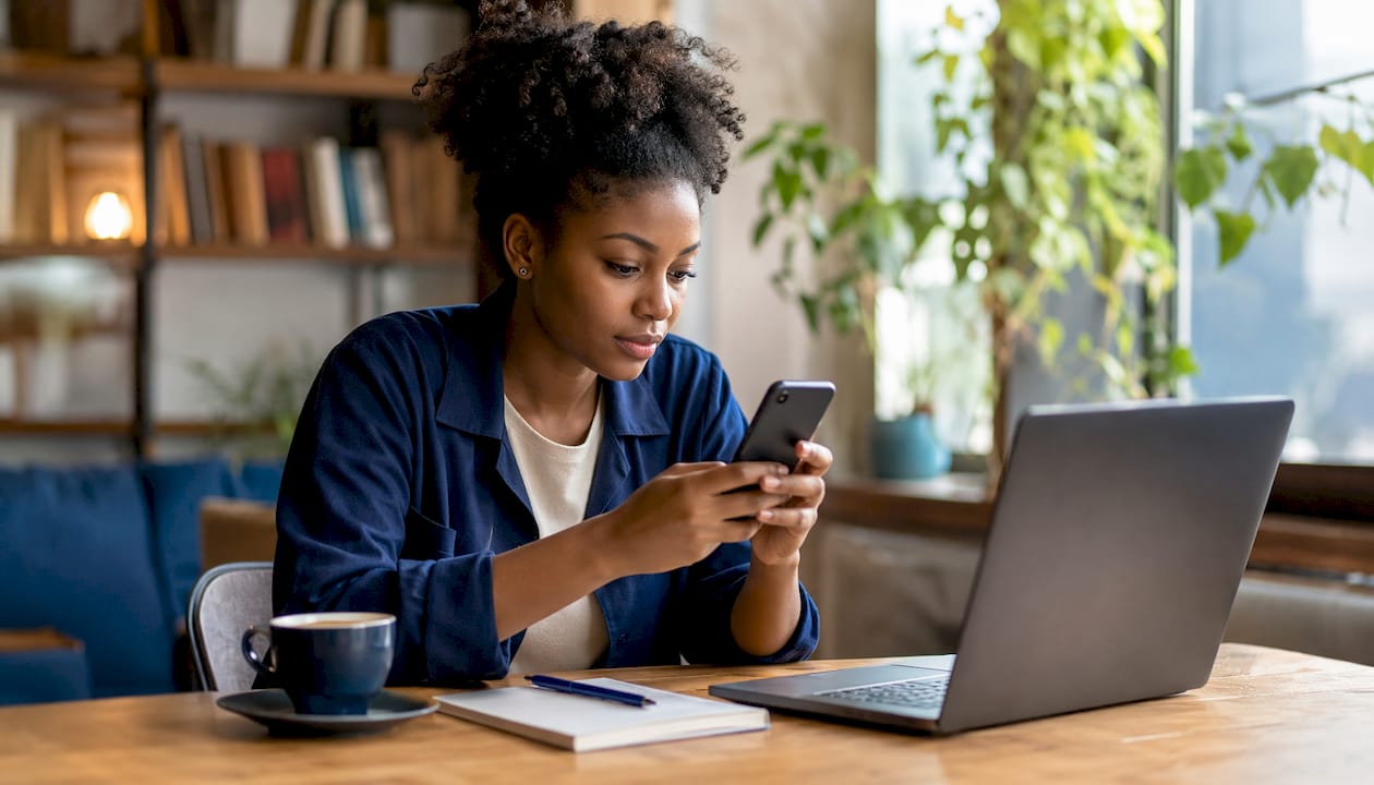 Une femme se connecte à FranceConnect depuis son smartphone, installée à son bureau.