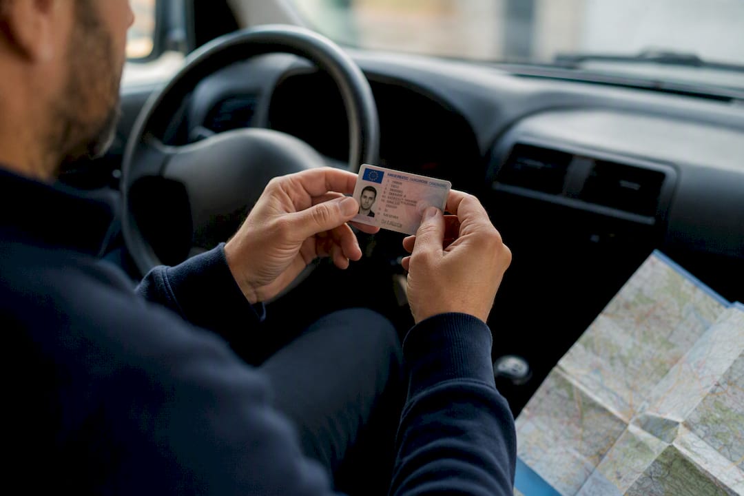 Des mains tiennent un permis de conduire français accompagné d'une enveloppe.