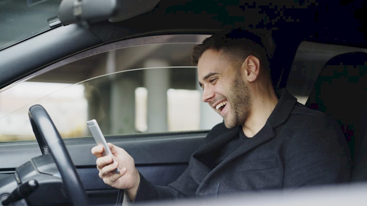 Smiling man looking at his phone in car