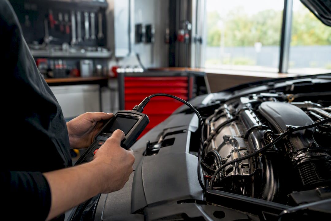 Technician hands using car diagnostic tool in engine bay