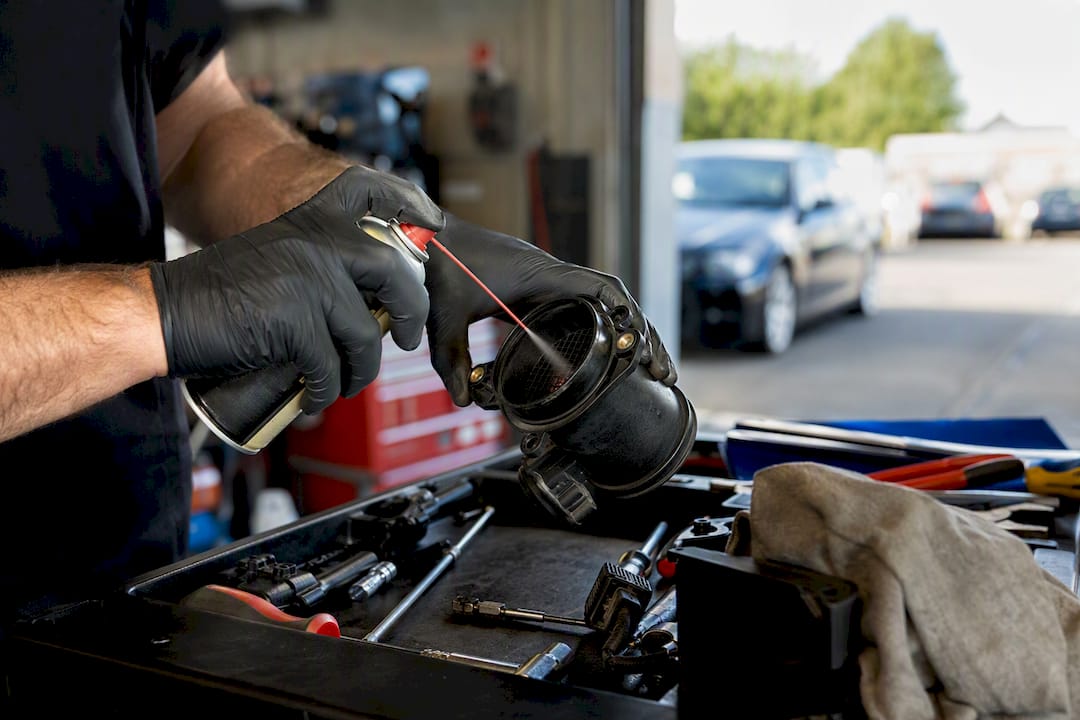 Hands cleaning a car's MAF sensor in workshop