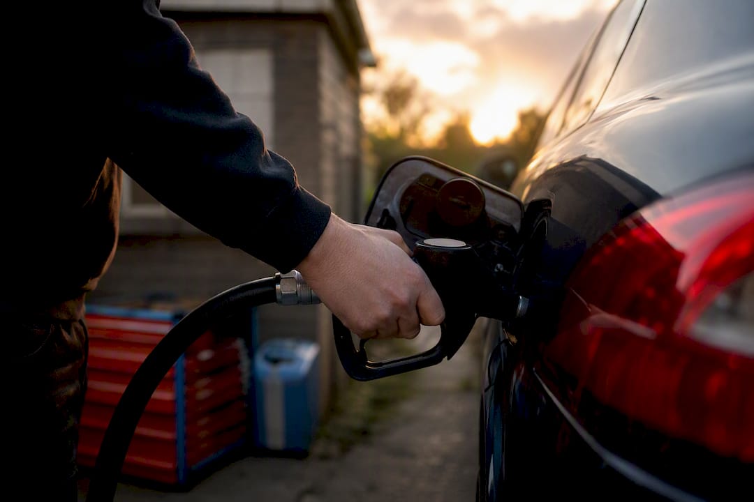 Hand holding fuel nozzle near anonymous engine bay