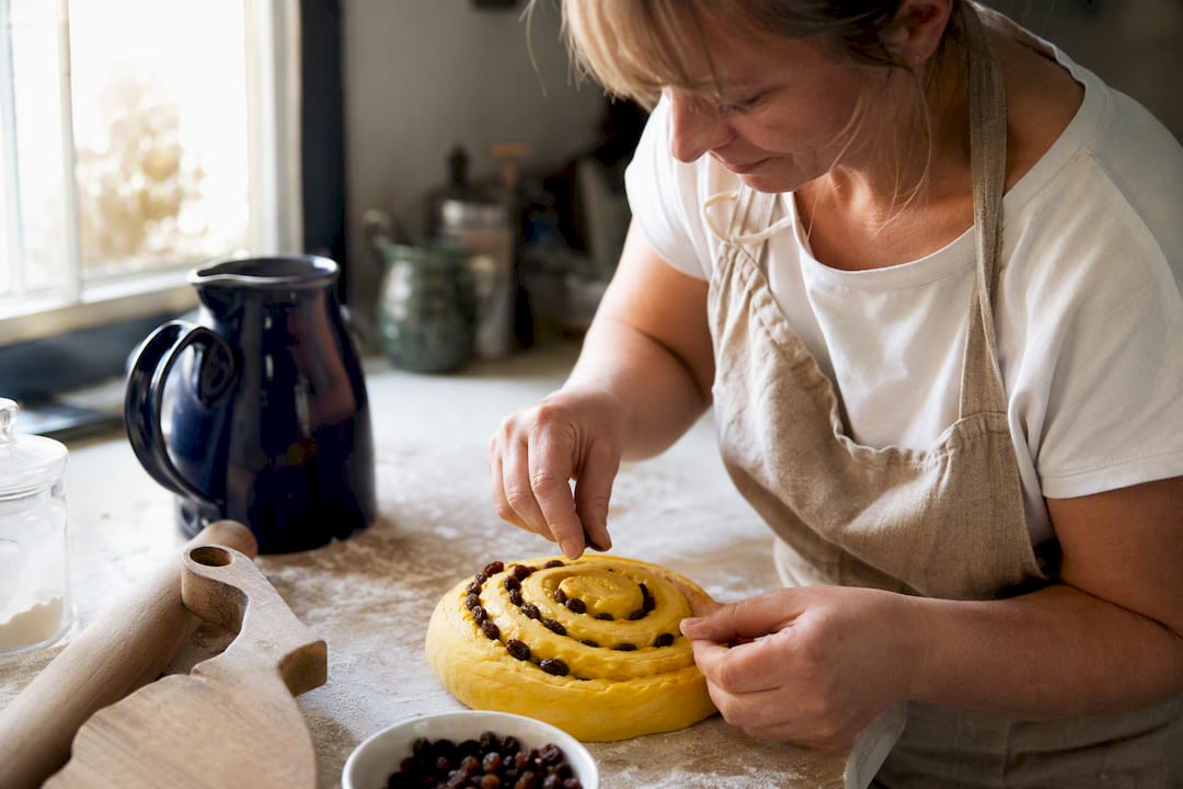 Hand pushing raisins into saffron bun dough