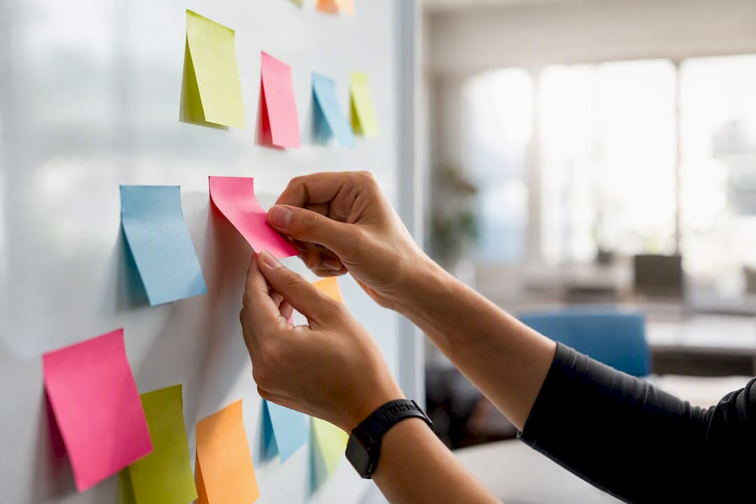 Hands arranging prioritization notes on glass board