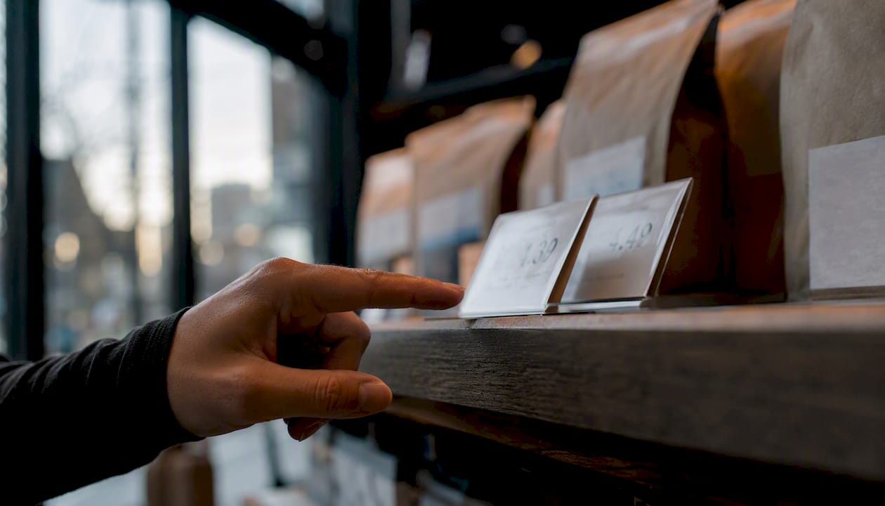 Hand pointing at different price tags on shelf