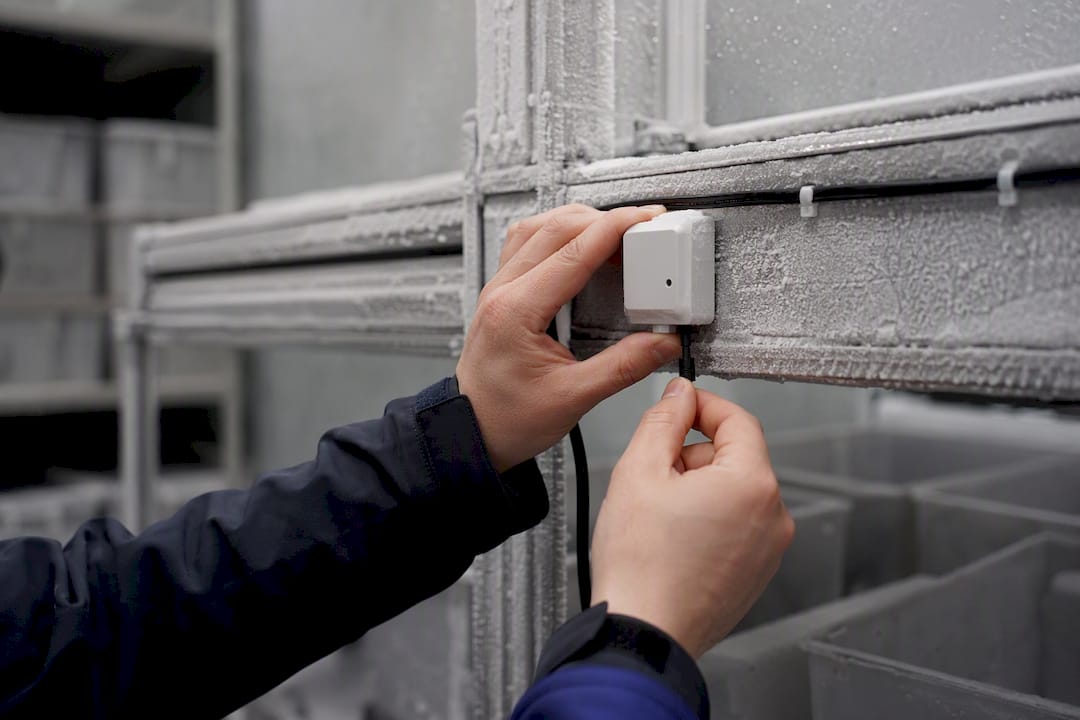Hands fitting IoT temperature sensor in warehouse