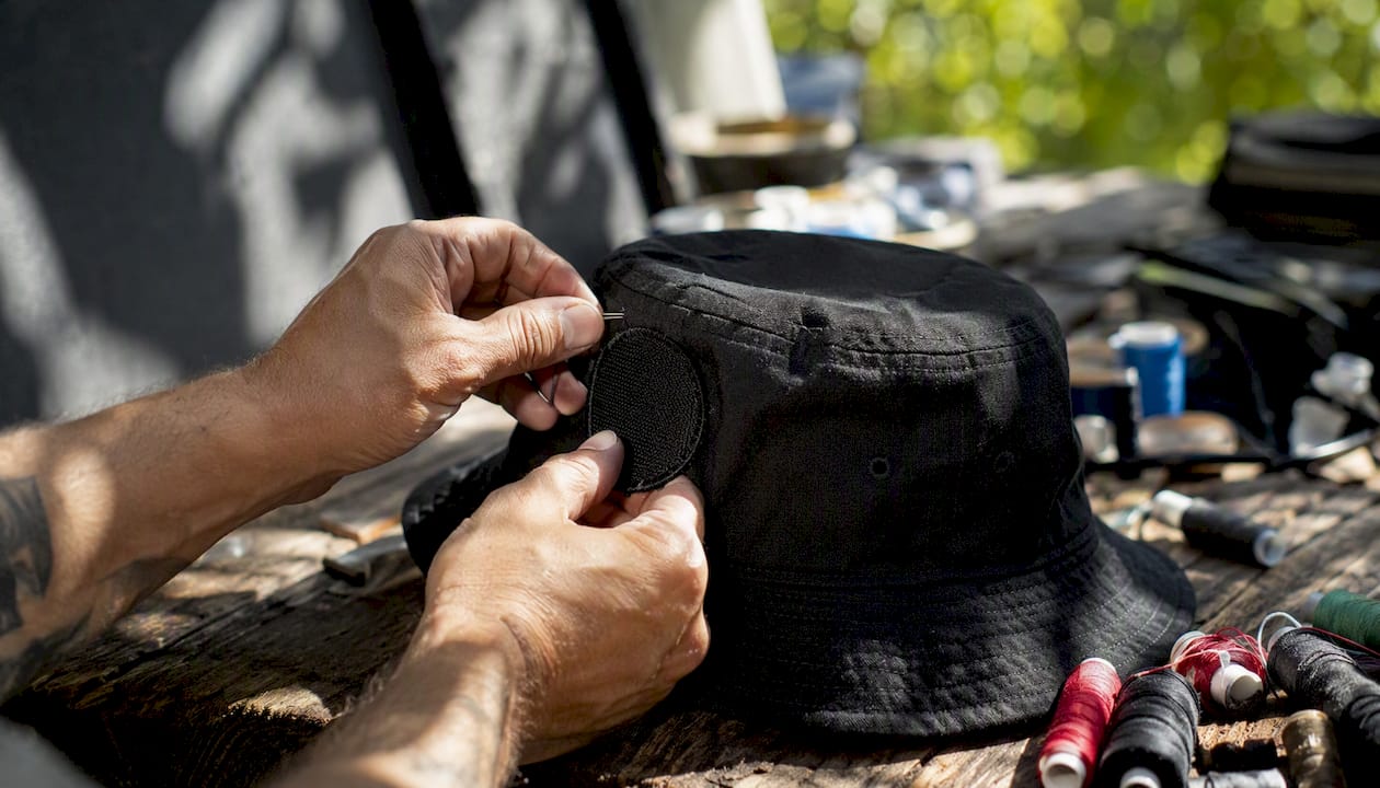Hands sewing patch on bucket hat side panel
