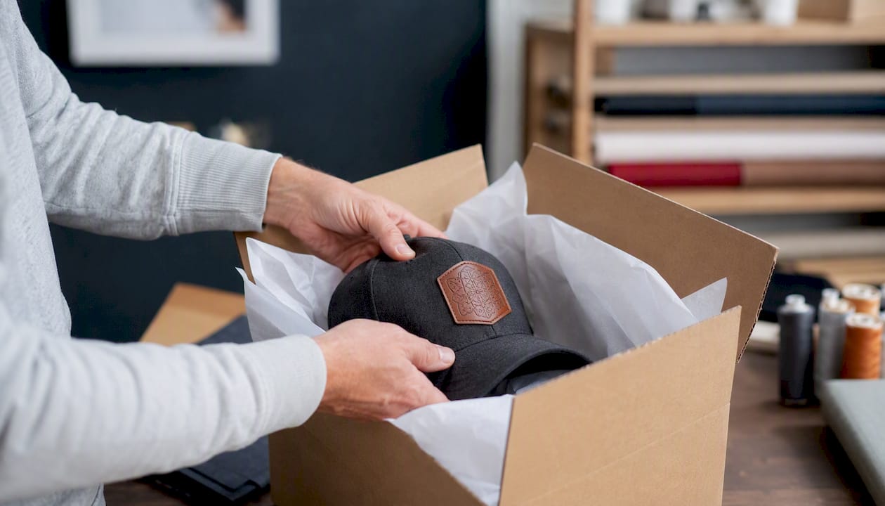 Hands packing patched hat with tissue lining box