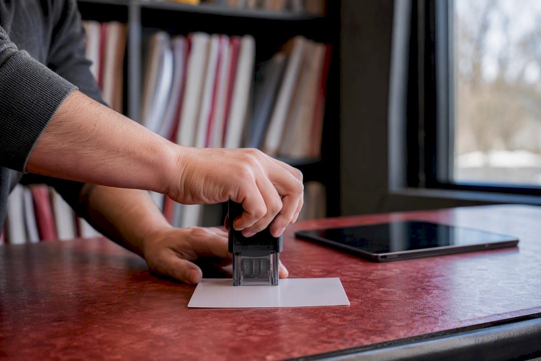 Hands date-stamping document with digital device nearby