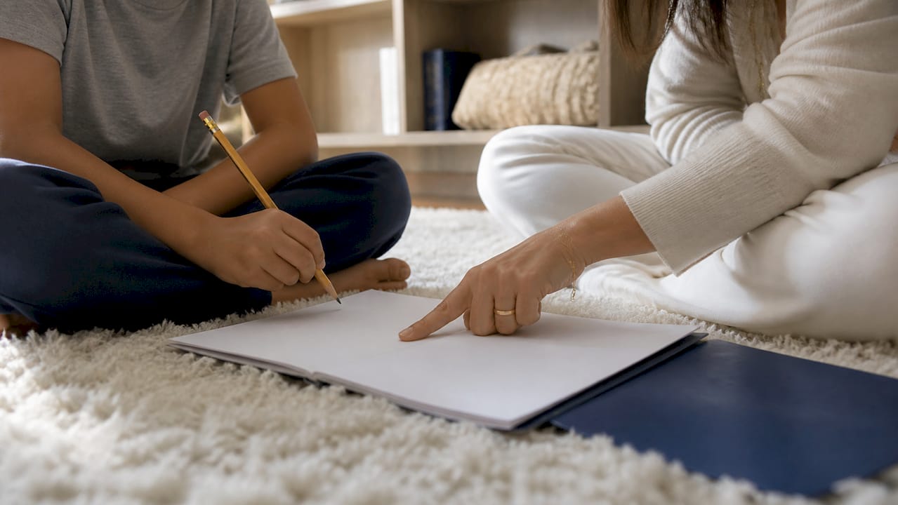 Un parent accompagne son enfant pour faire ses devoirs à la maison, installé ensemble à leur bureau.