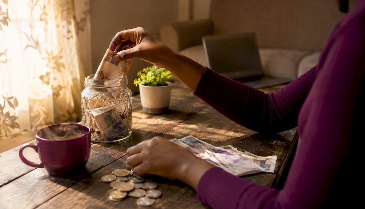 Hands placing Naira into savings jar