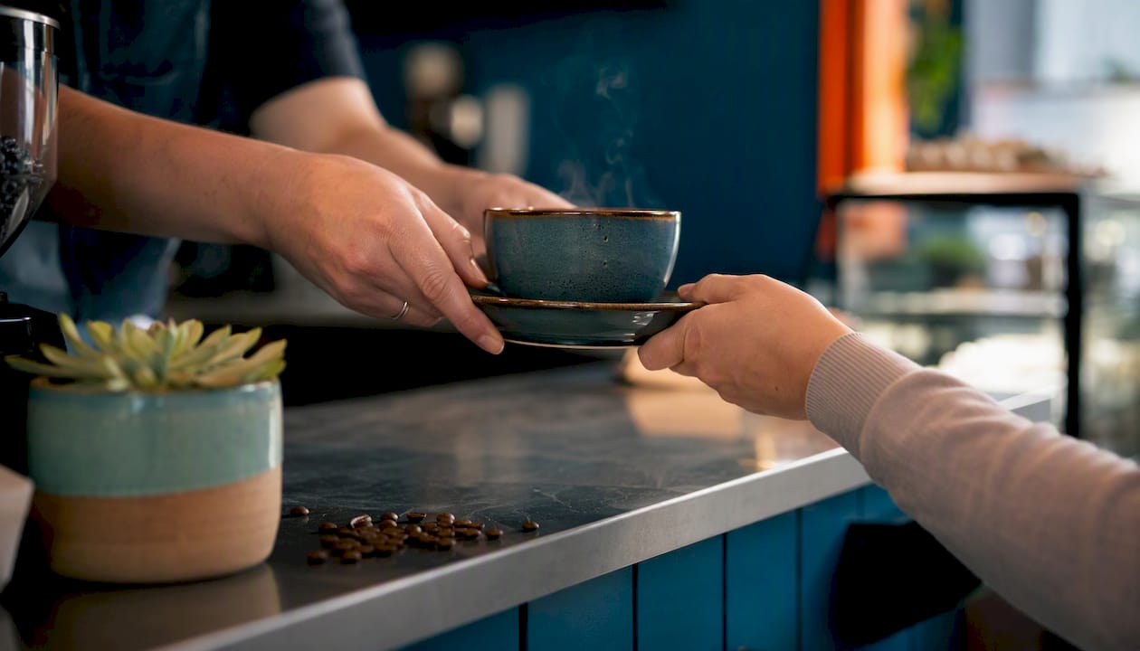 Hand receiving steaming coffee cup at pickup