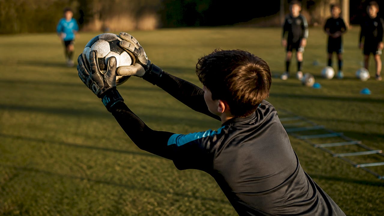 Nachwuchstorwart schnappt sich den Ball sicher mit Handschuhen mit Fingerschutz.