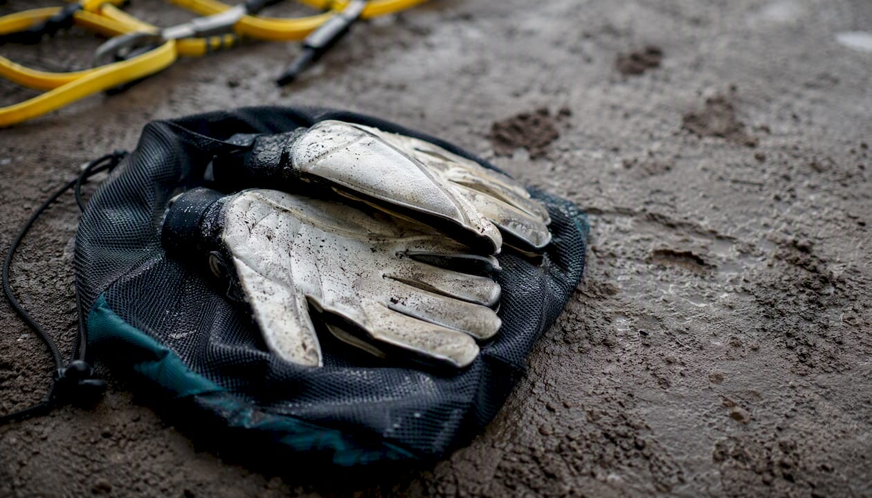 Nasse Handschuhe hängen zum Trocknen an einer Sporttasche aus Netzstoff im Freien.