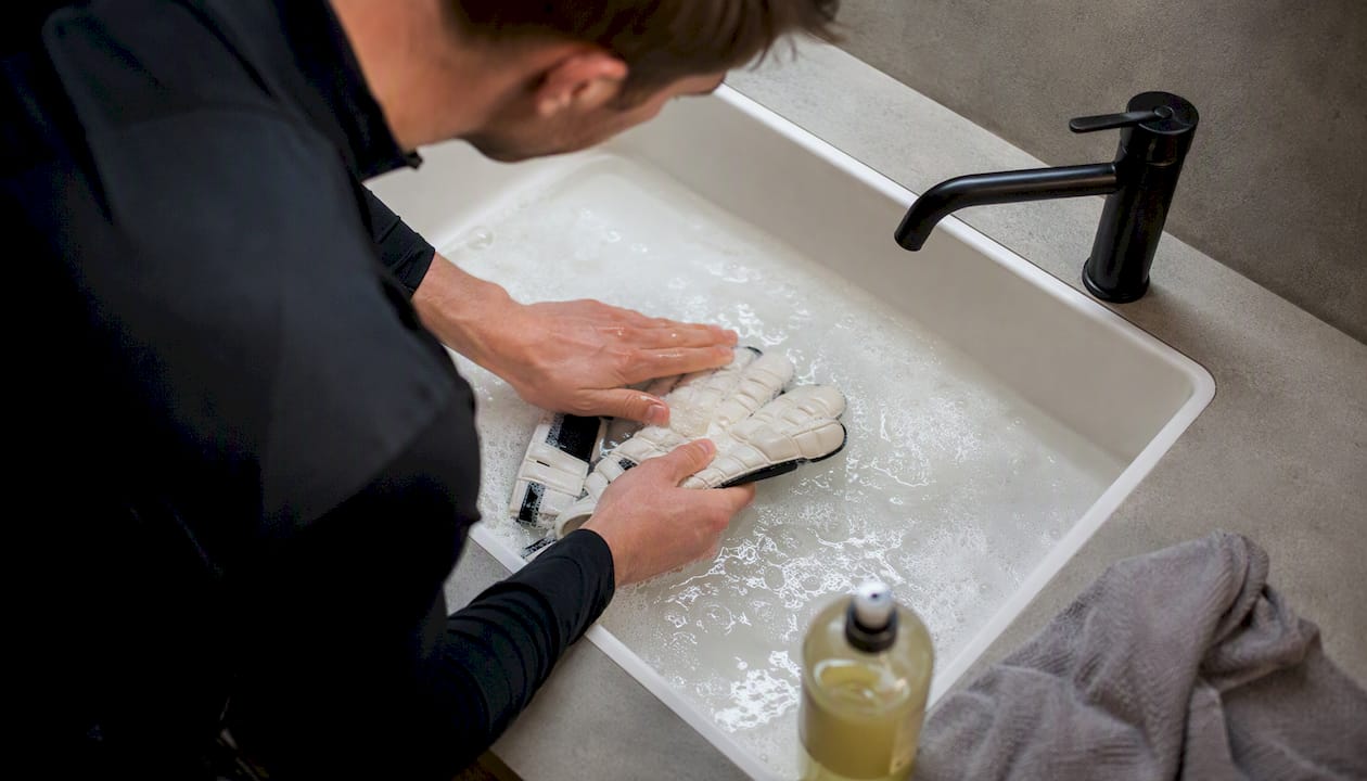Mit sanften Bewegungen werden Torwarthandschuhe behutsam in einem Wasserbecken gereinigt.