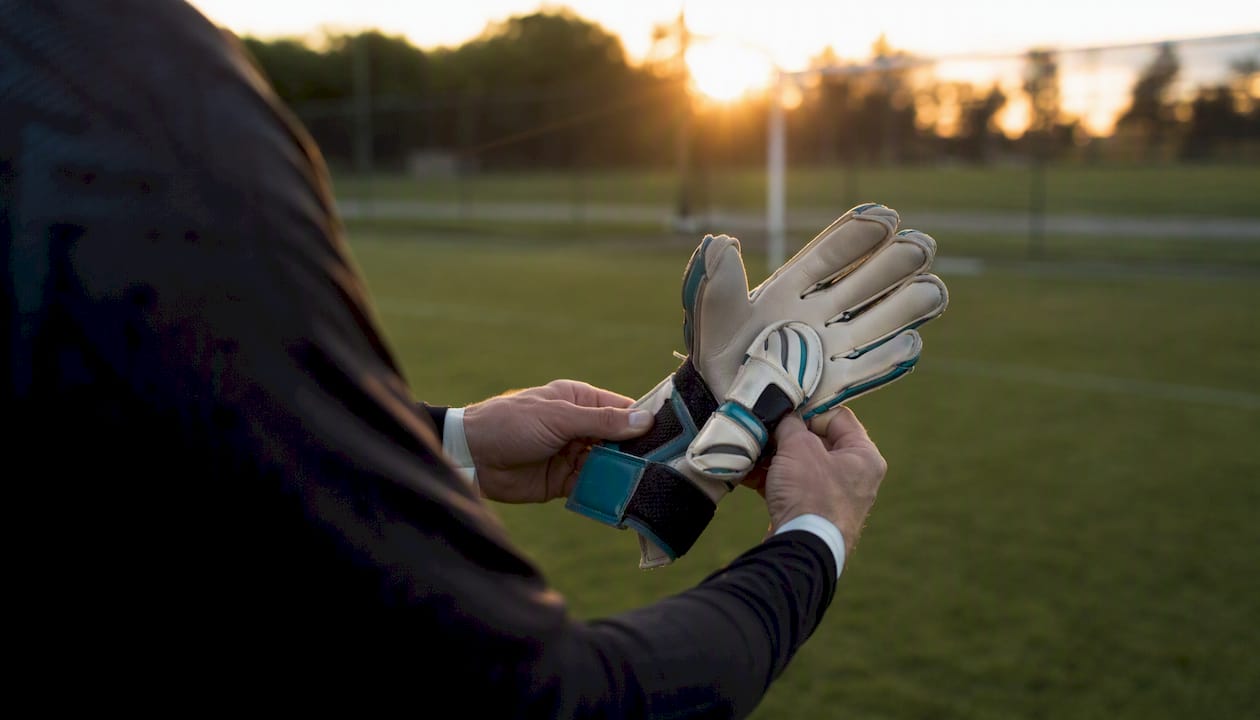 Der Torwart überprüft sorgfältig die Nähte und Verschlüsse seiner Handschuhe, um sicherzugehen, dass sie einwandfrei sitzen und beim Spiel optimalen Halt bieten.