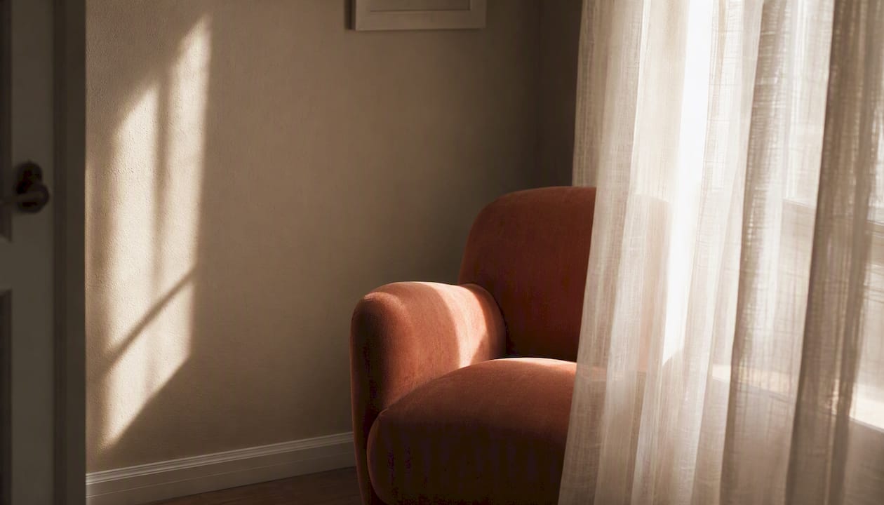 Softly lit empty armchair behind sheer curtains